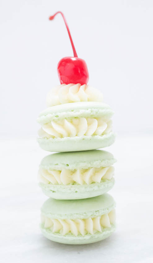 Three Shamrock Shake Macarons stacked on top of one another with a cherry on top.