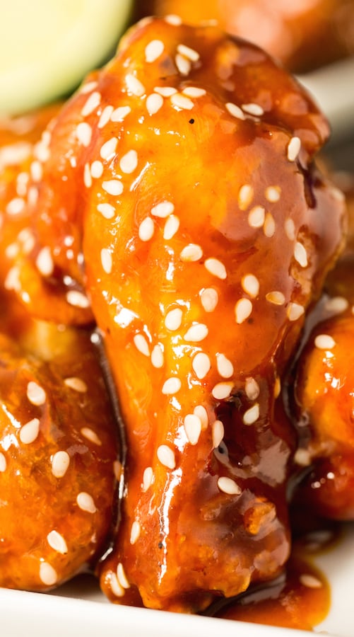 An extreme close up of a drumette wing covered in the orange sriracha honey lime sauce and white sesame seeds as garnish.