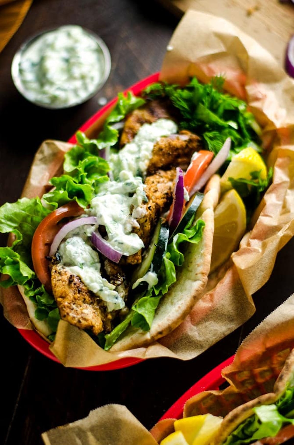 A plastic food basket has been lined with brown paper and a homemade gyro has been place on top with lemon wedges on the side.