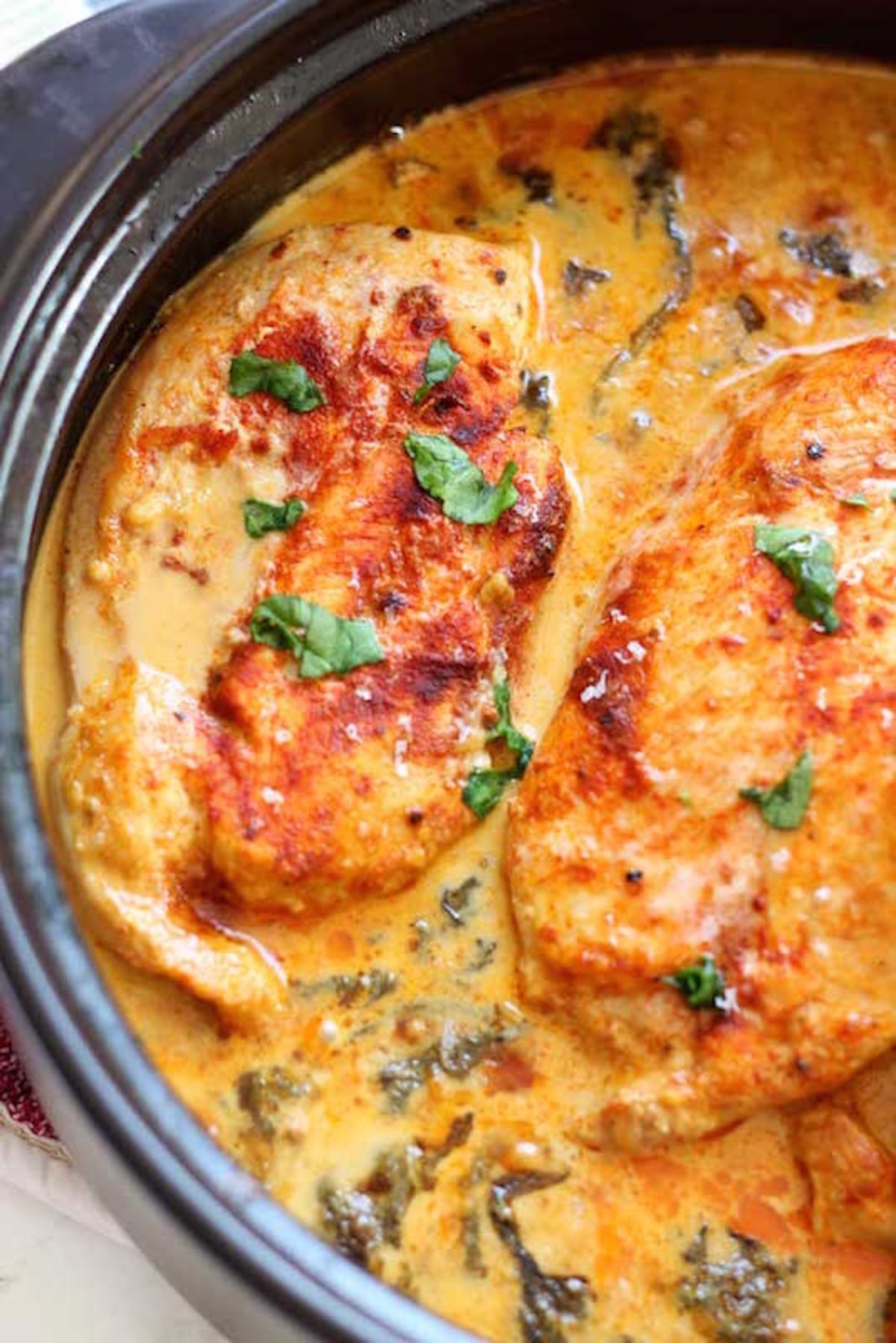 A skillet is filled with chicken breasts that have been seared, then cooked in a light orange lemon butter sauce.