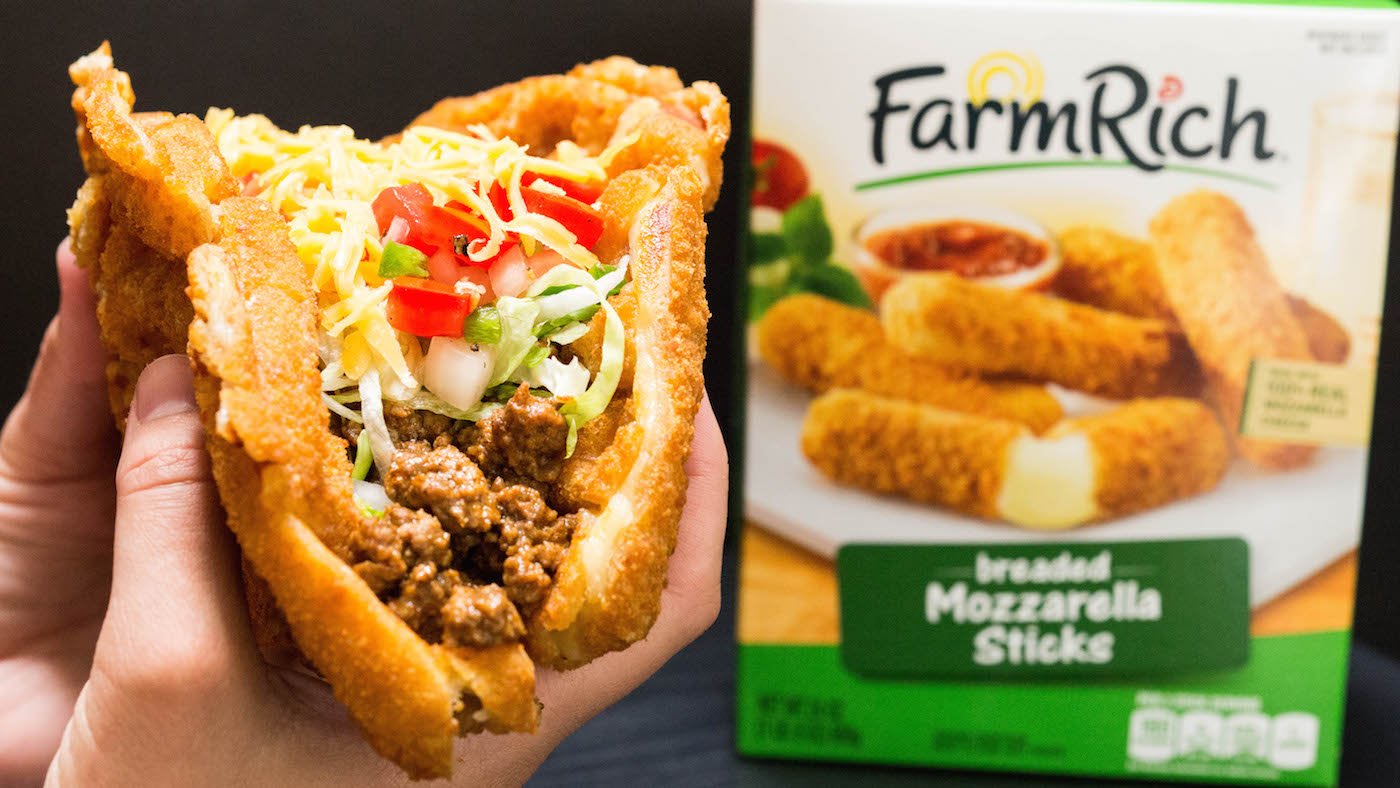 A hand holds up a Waffled Mozzarella Stick Taco in front of a Farm Rich Mozzarella Stick Box.