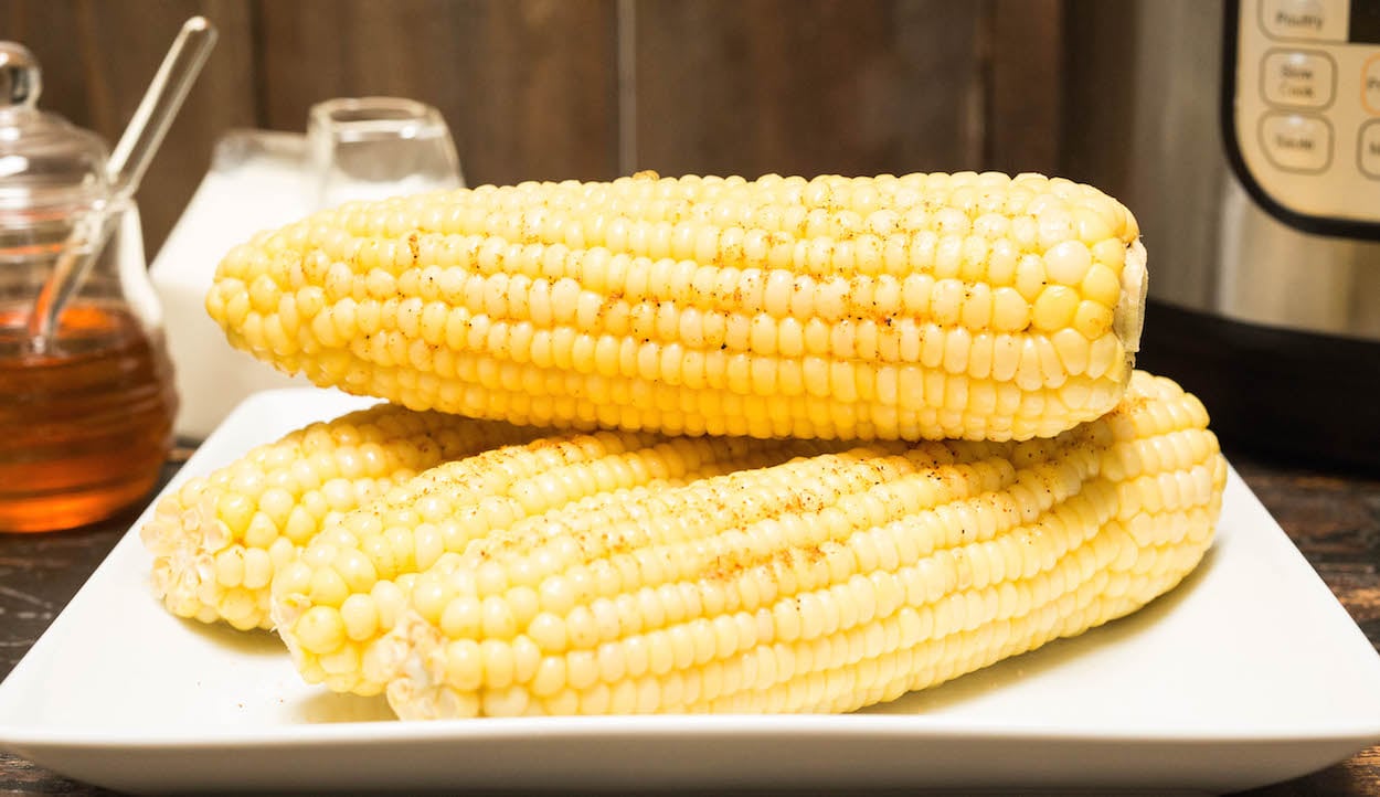 Ears of corn that have been cooked in the Instant Pot. A jar of any and milk are in the background.