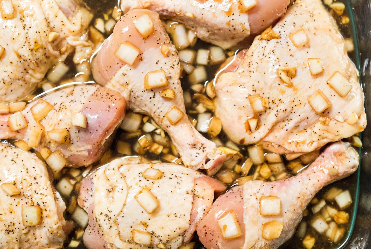 Raw chicken in a baking dish covered in marinade with chopped onions.