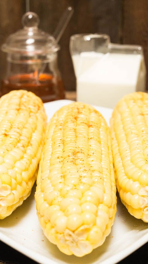 Three ears of Instant Pot corn in front of glass honey & milk jars.