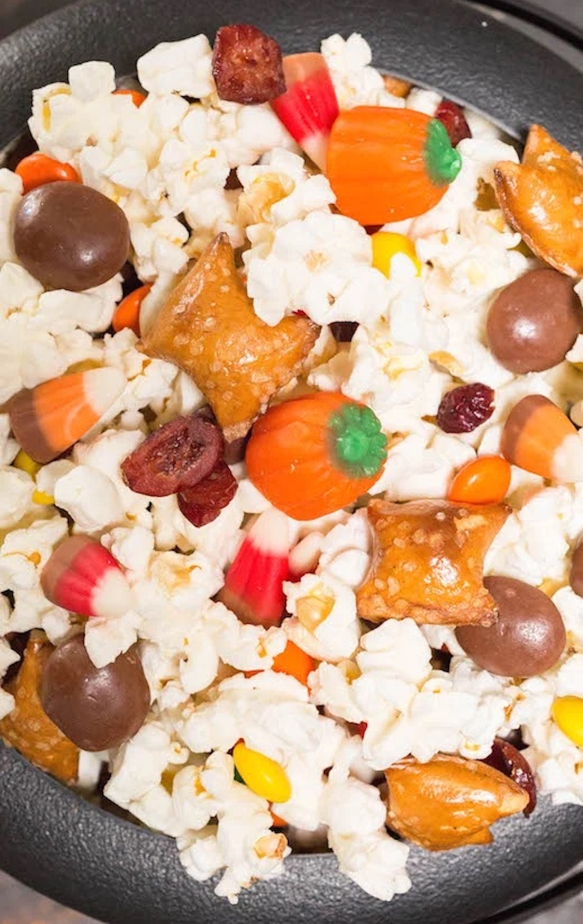 Close up of Halloween Movie Snack Mix filled with popcorn, candy pumpkins, candy corn, peanut butter filled pretzels, and milk duds.