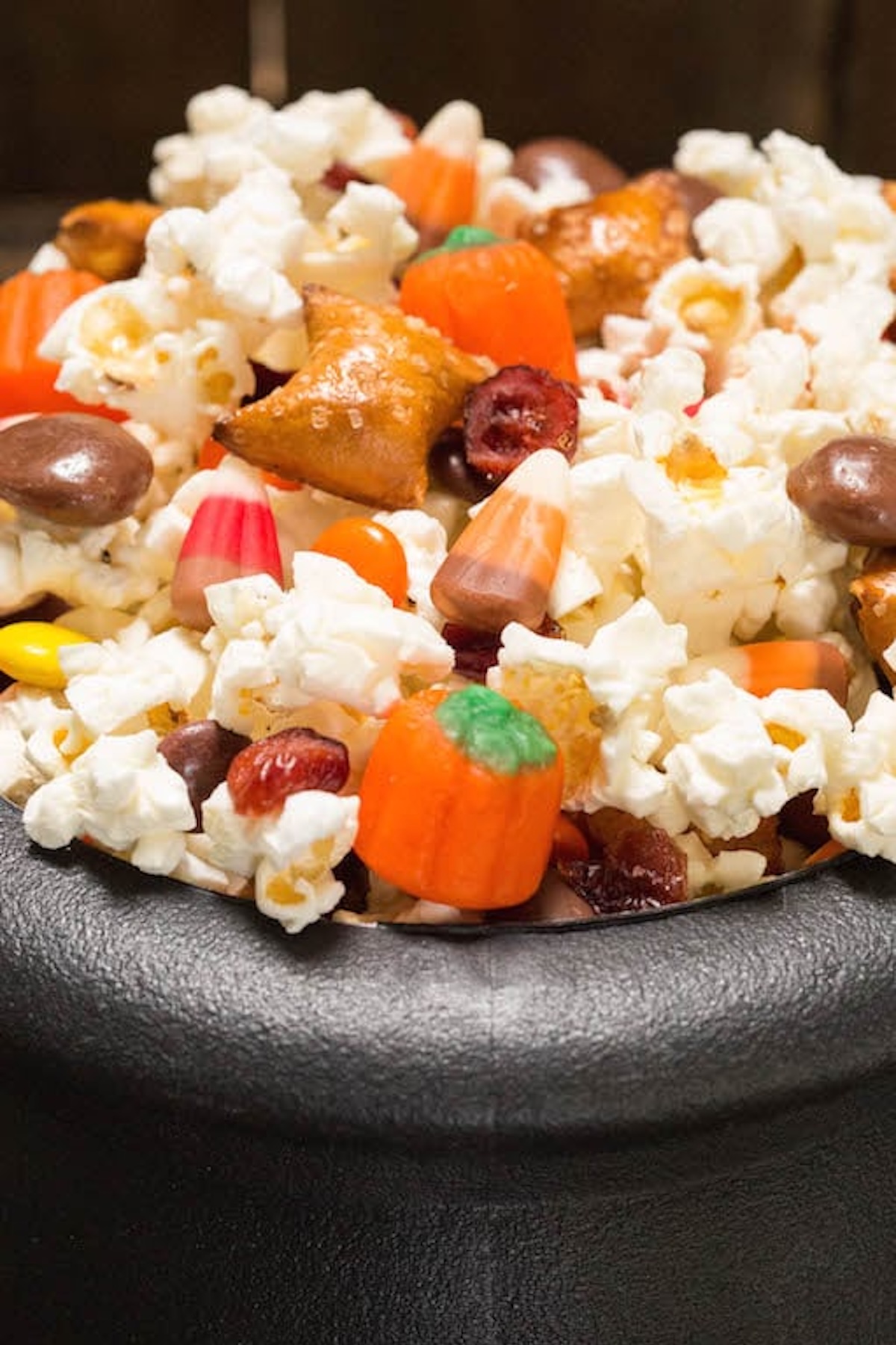 A plastic cauldron filled with Halloween Snack Mix with popcorn, candy corn, pumpkin candies, cranberries, peanut butter filled pretzels, and milk duds.