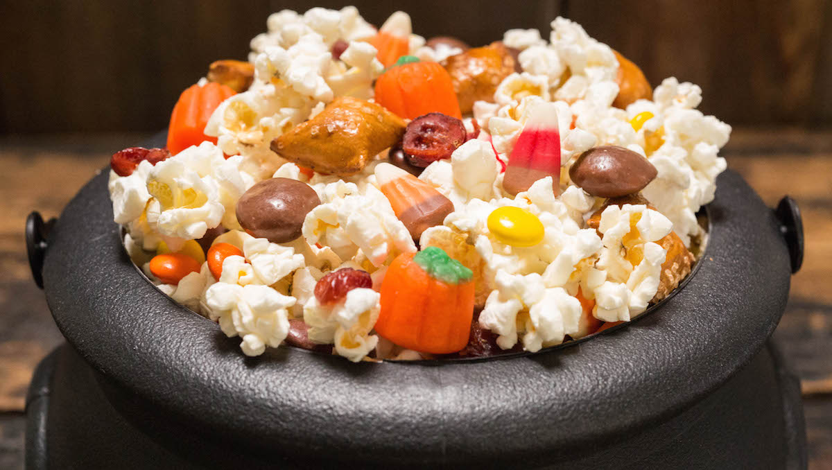 A plastic cauldron filled with Halloween Snack Mix comprised of popcorn and fall candy.