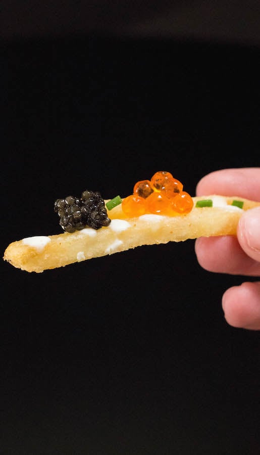 Close up of a single French fry with black caviar, and orange roe caviar on top.