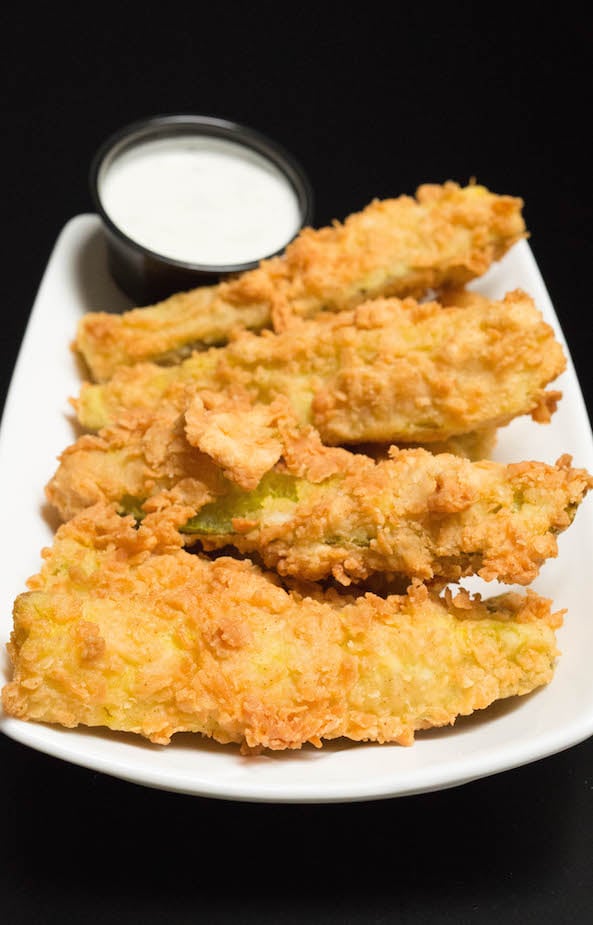 Breaded Fried Pickle Spears in a white serving dish next to ranch.