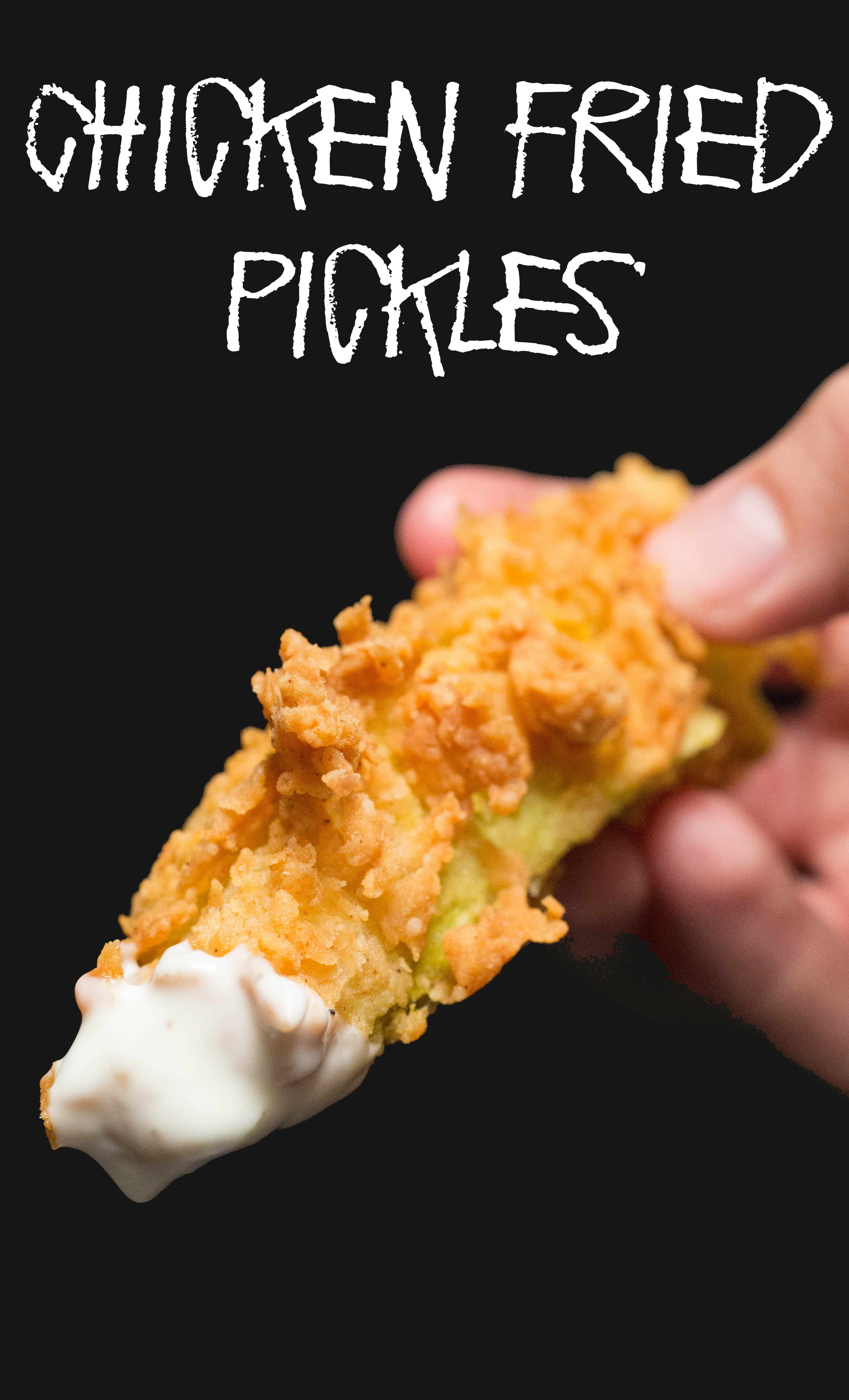 Close up of hand holding up a fried pickle that's been dipped in ranch. Text at the top reads "chicken fried pickles".