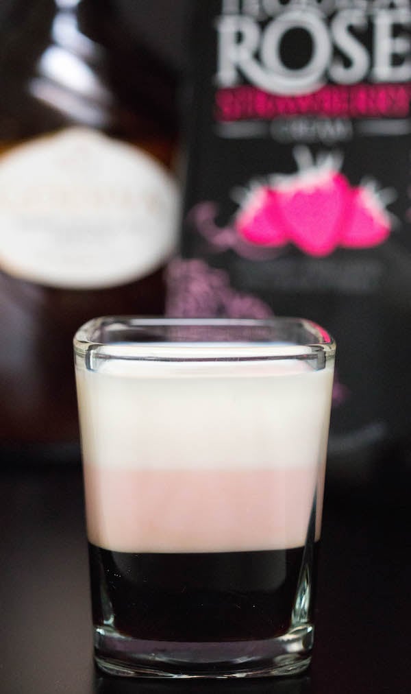 A layered Neapolitan shot with Tequila Rose and Godiva White Chocolate Liqueur in the background.