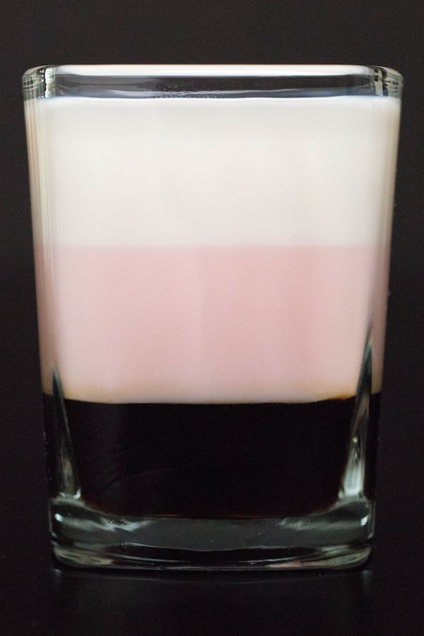 Close up of a Neapolitan Shot featuring a dark brown layer, a pink layer, and a white layer.
