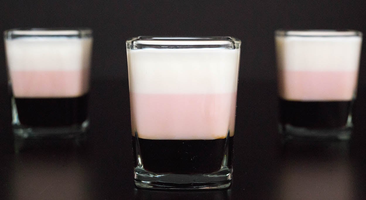 Three layered Neapolitan Shots in square shot glasses on a black background.