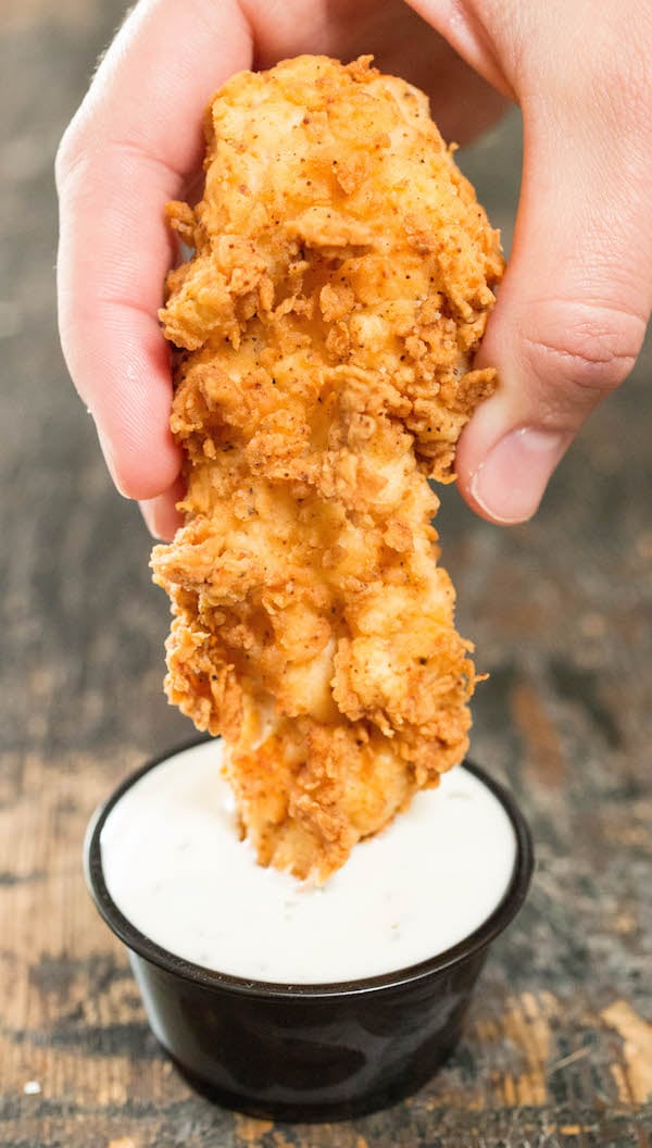 Buttermilk chicken tender being dipped in ranch dressing.