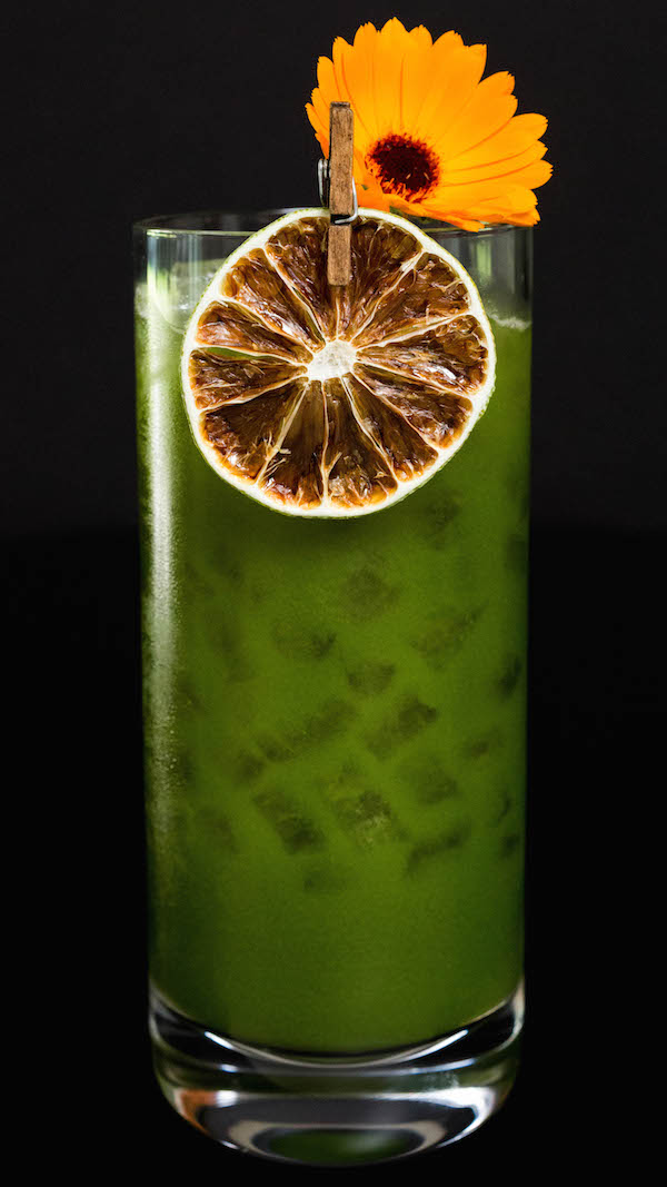 A Green Juice Margarita that's garnished with a dehydrated lime wheel and an orange edible flower.