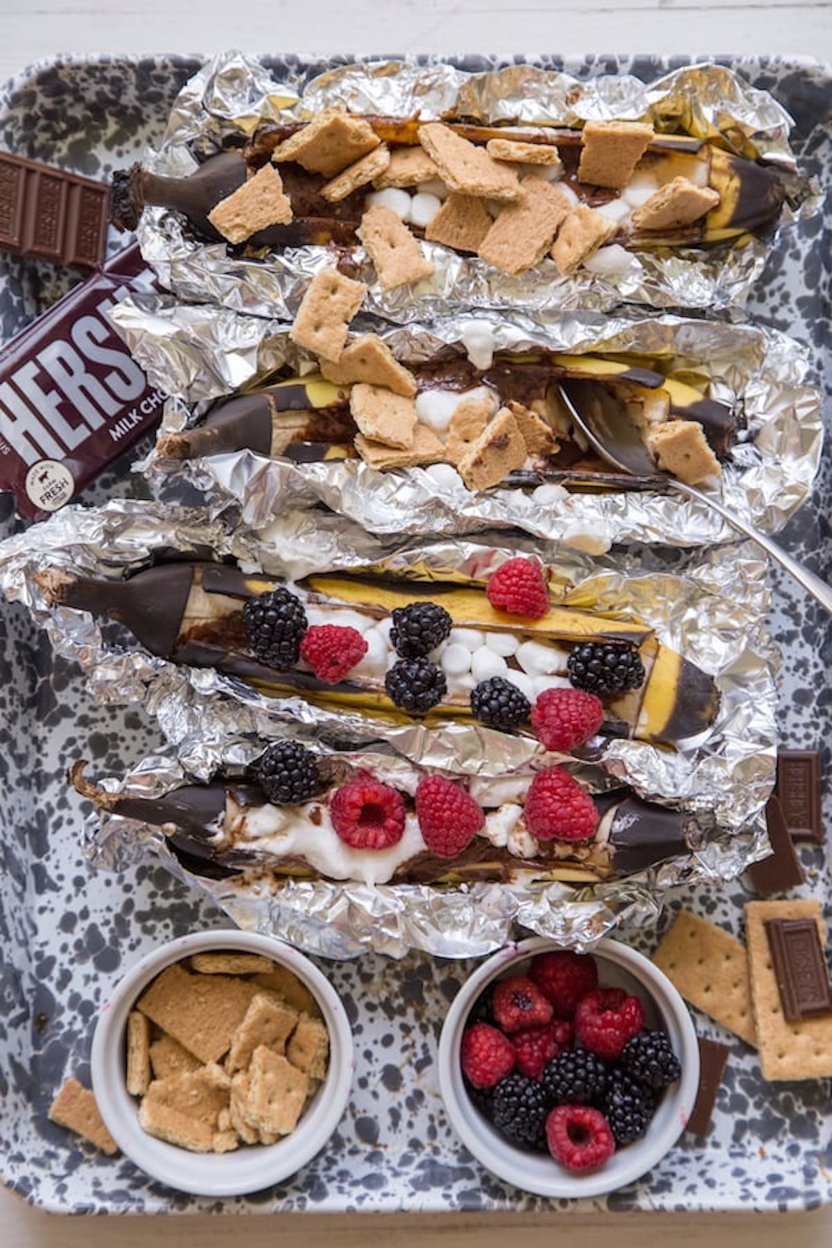 Grilled banana that have been sliced open and stuffed with chocolate, mini marshmallows, and fresh berries. A bar of Hershey's milk chocolate is off to the side.