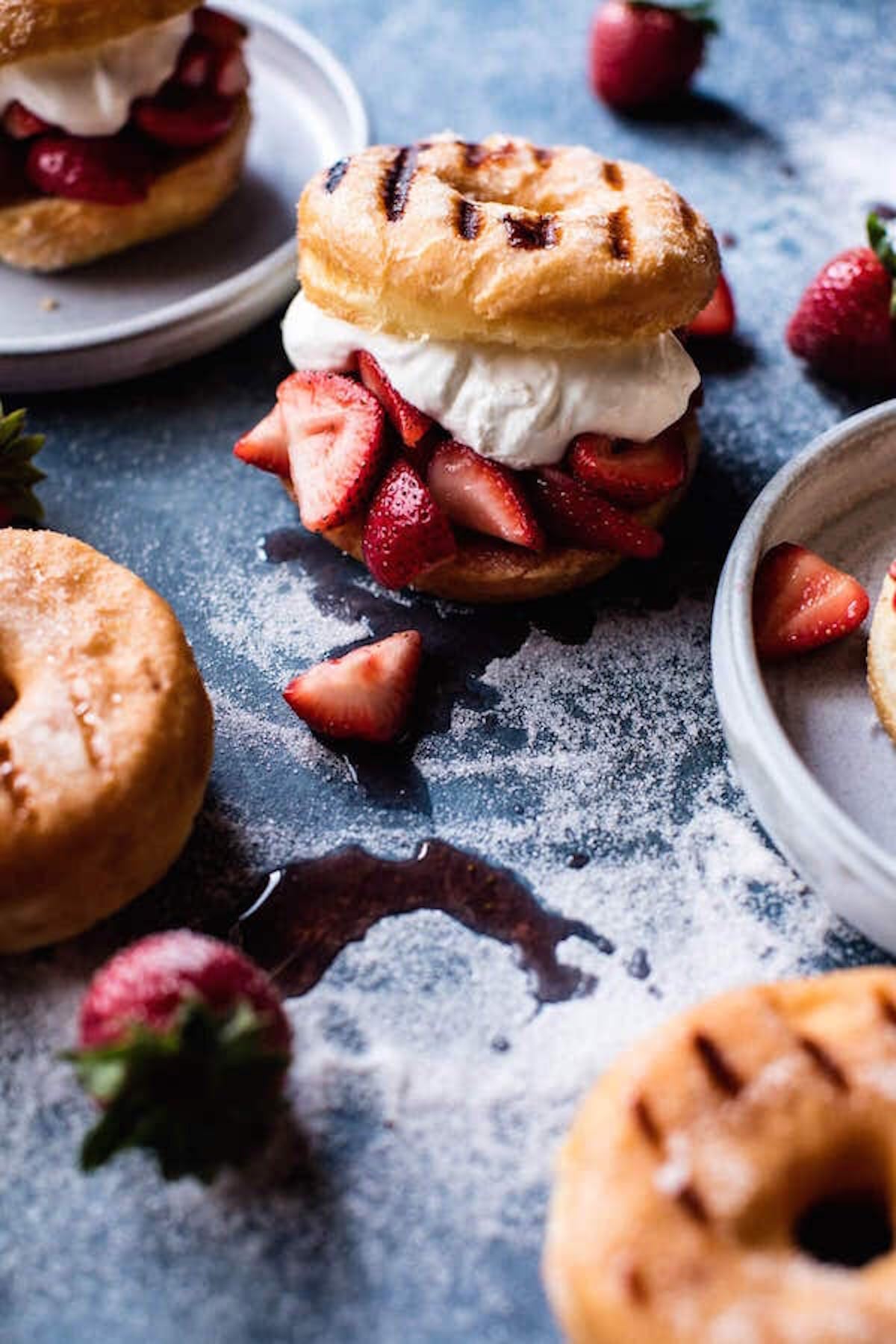 Grilled glazed donuts that have been split in half and filled with sliced strawberries and a generous dollop of cream.
