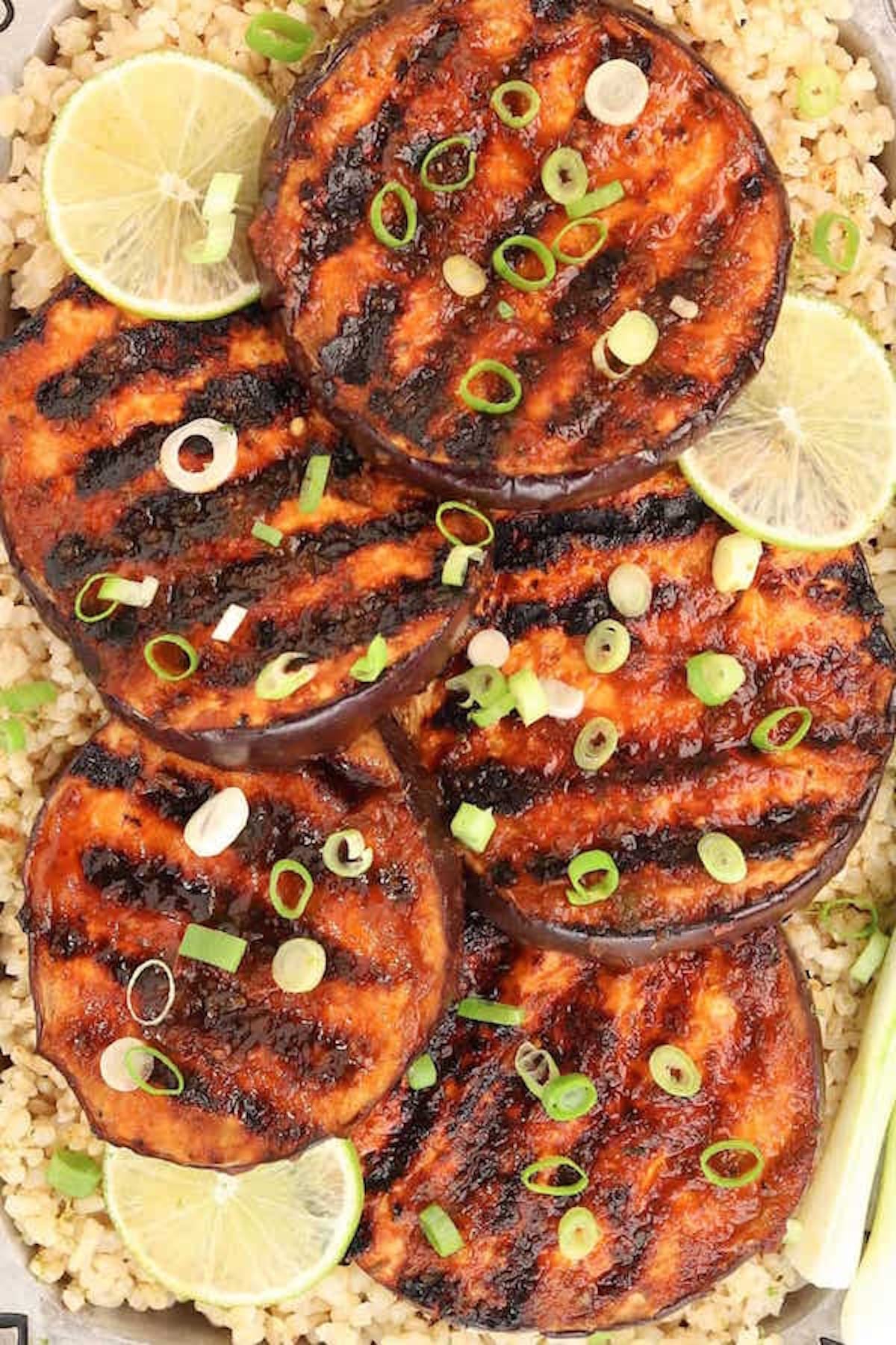 Sliced eggplant with visible grill marks topped with sliced green onion. Sliced limes on the side.