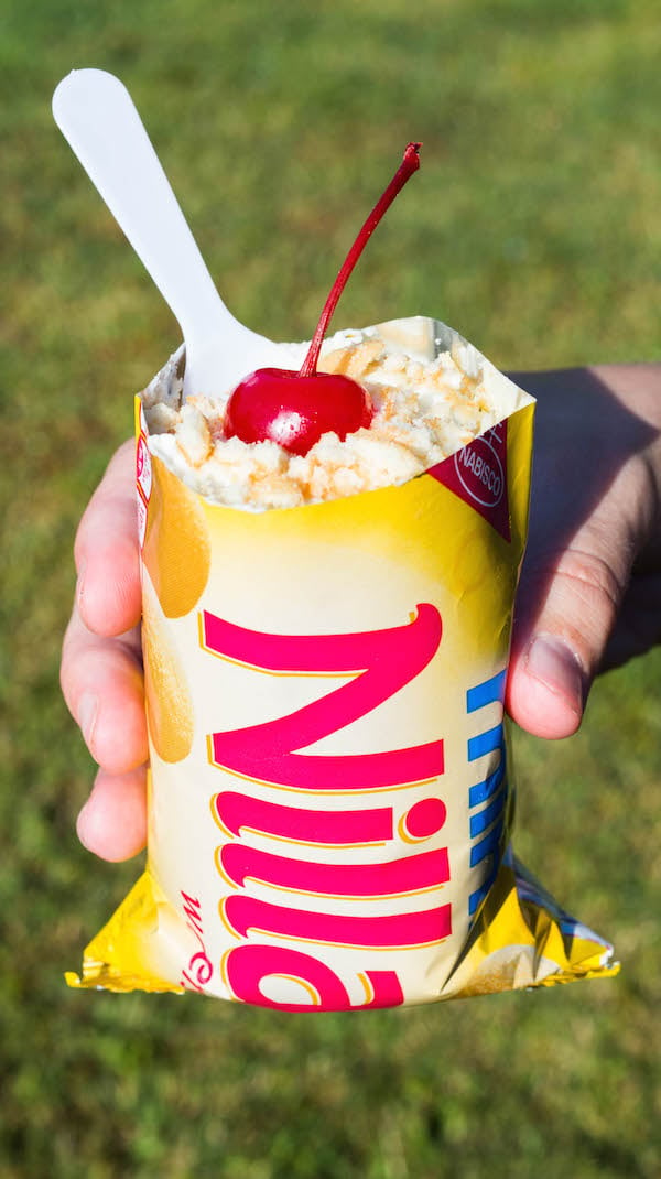 A hand holds up a Portable "Walking" Banana Pudding in a Nilla Wafers Bag in a backyard.