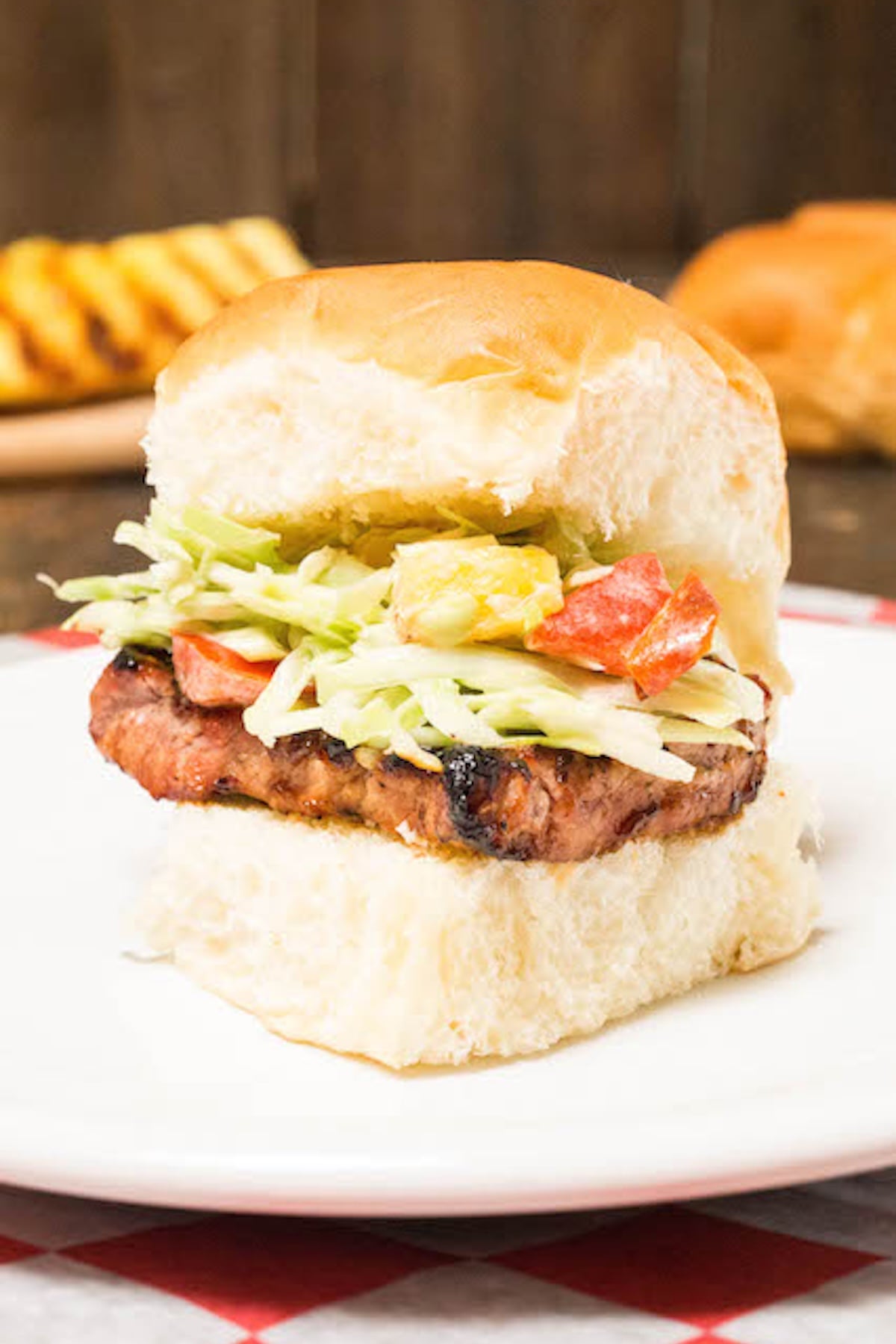 A Hawaiian roll is filled with a sliced of grilled pork tenderloin that's topped with a Cole slaw that has grilled chunks of pineapple and red pepper.