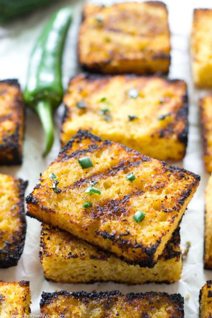 Pieces of square, grilled corn bread are stacked on top of one another and garnished with chives.