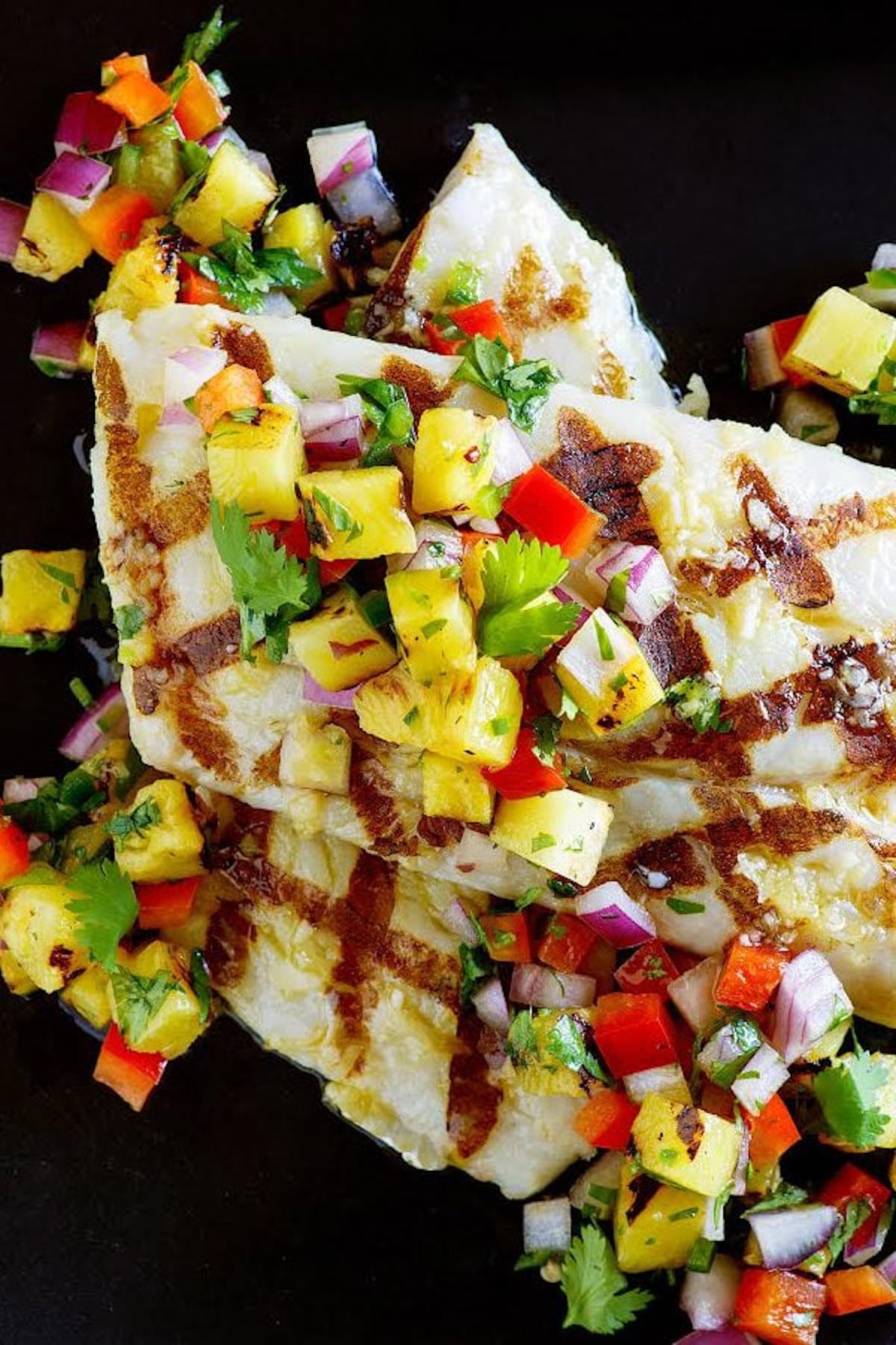 Grilled pieces of mahi mahi are topped with chopped grilled pineapple, peppers, onions, and cilarntro.