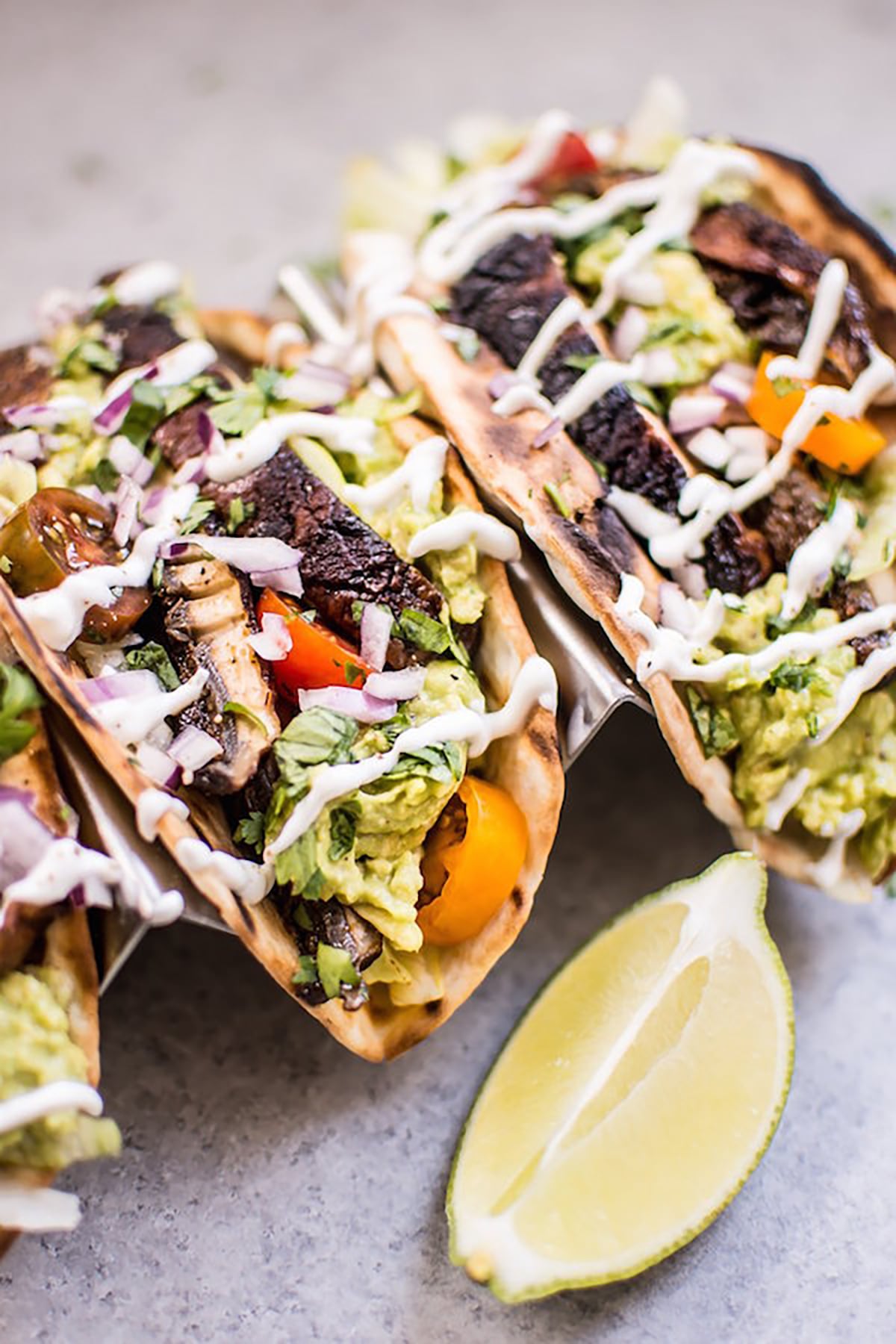 Two tacos in tortilla shells each filled with guacamole, grilled mushrooms, tomato, guacamole, and a drizzle of crema.