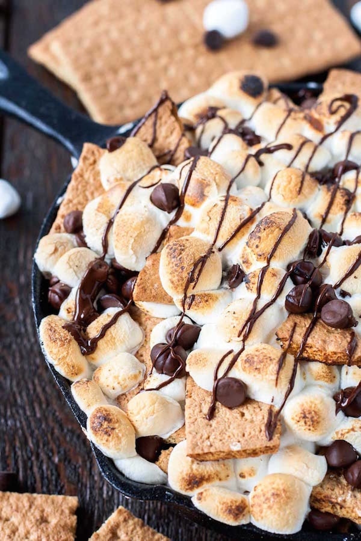 A cast iron skillet filled with graham crackers with toasted marshmallows, chocolate chips, and chocolate drizzle on top.