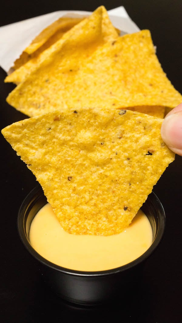 A chip being dipped in homemade Taco Bell nacho cheese.