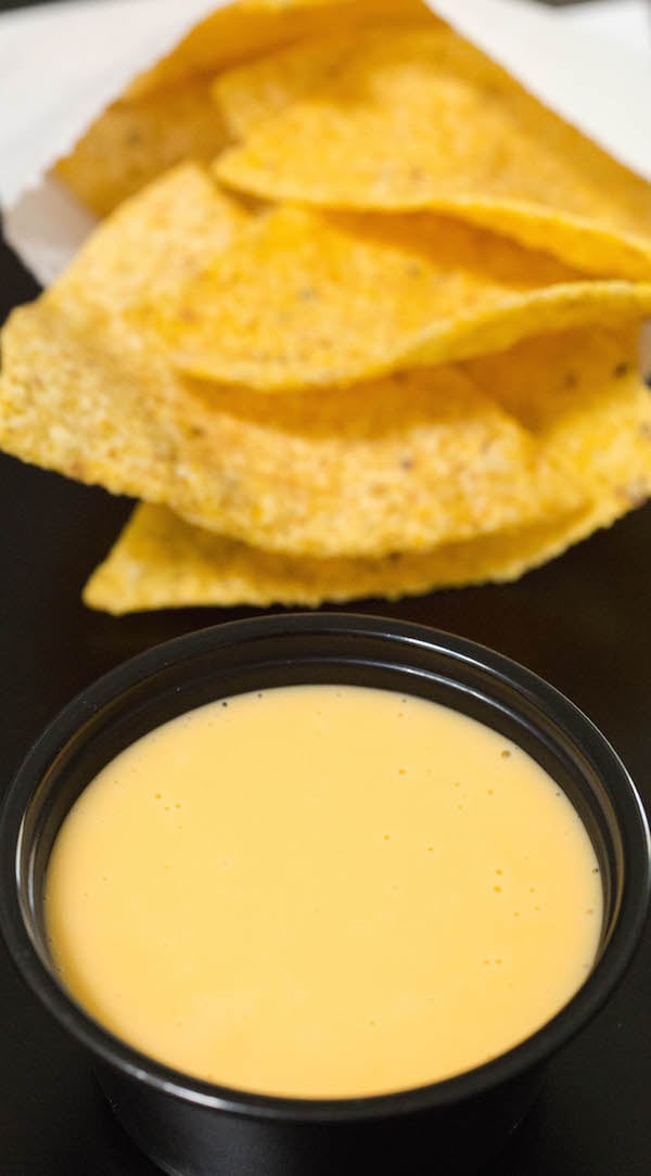 A small black cup of homemade Taco Bell Nacho Cheese in front of a bag of tortilla chips.