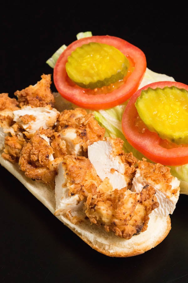 An open Chicken Tender Sub Sandwich showing the chopped chicken tenders on the bottom and the lettuce, tomato, pickles on top.