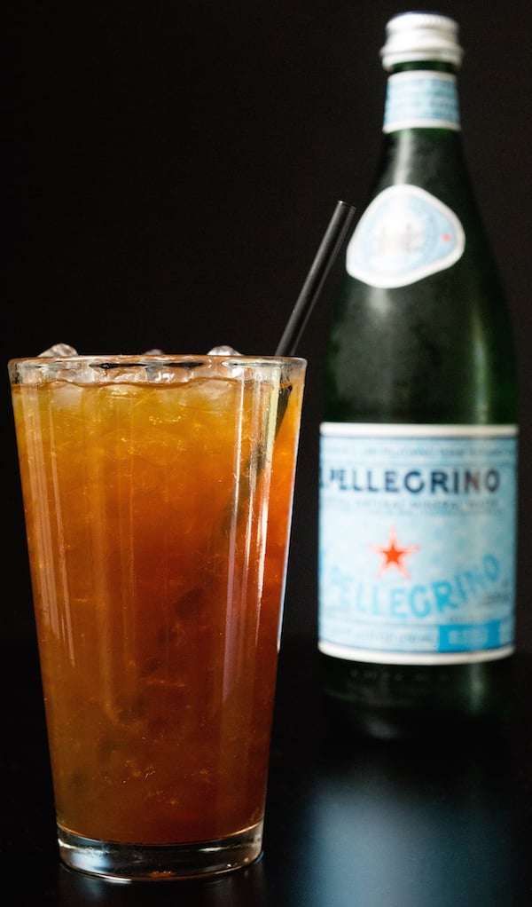 A sparkling coffee with a straw in front of a bottle of Pellegrino.