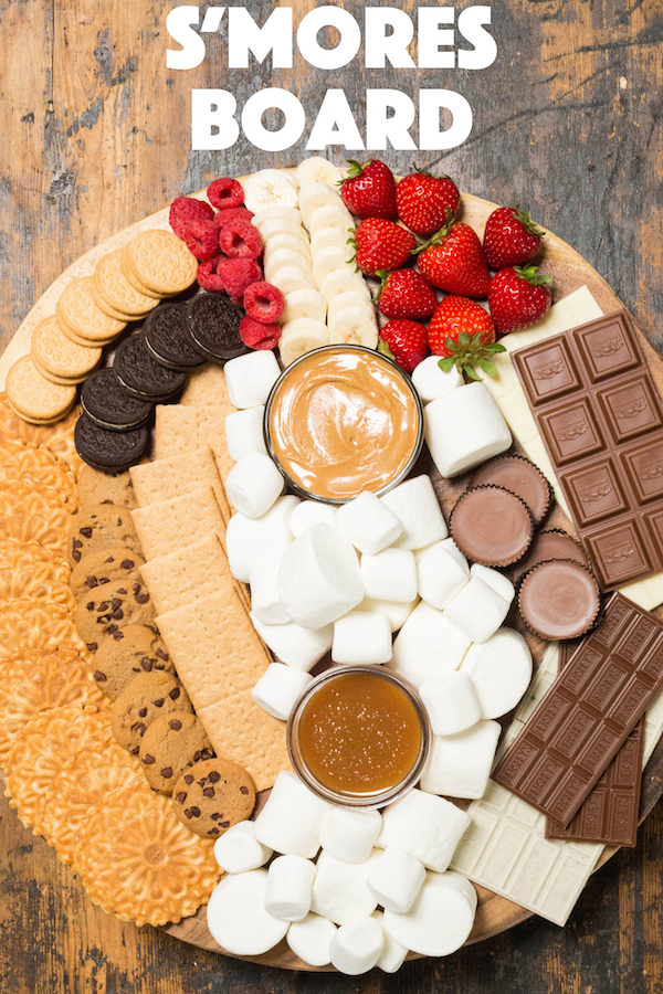 A large wooden board with various marshmallows, cookies, chocolates, and toppings to make s'mores.