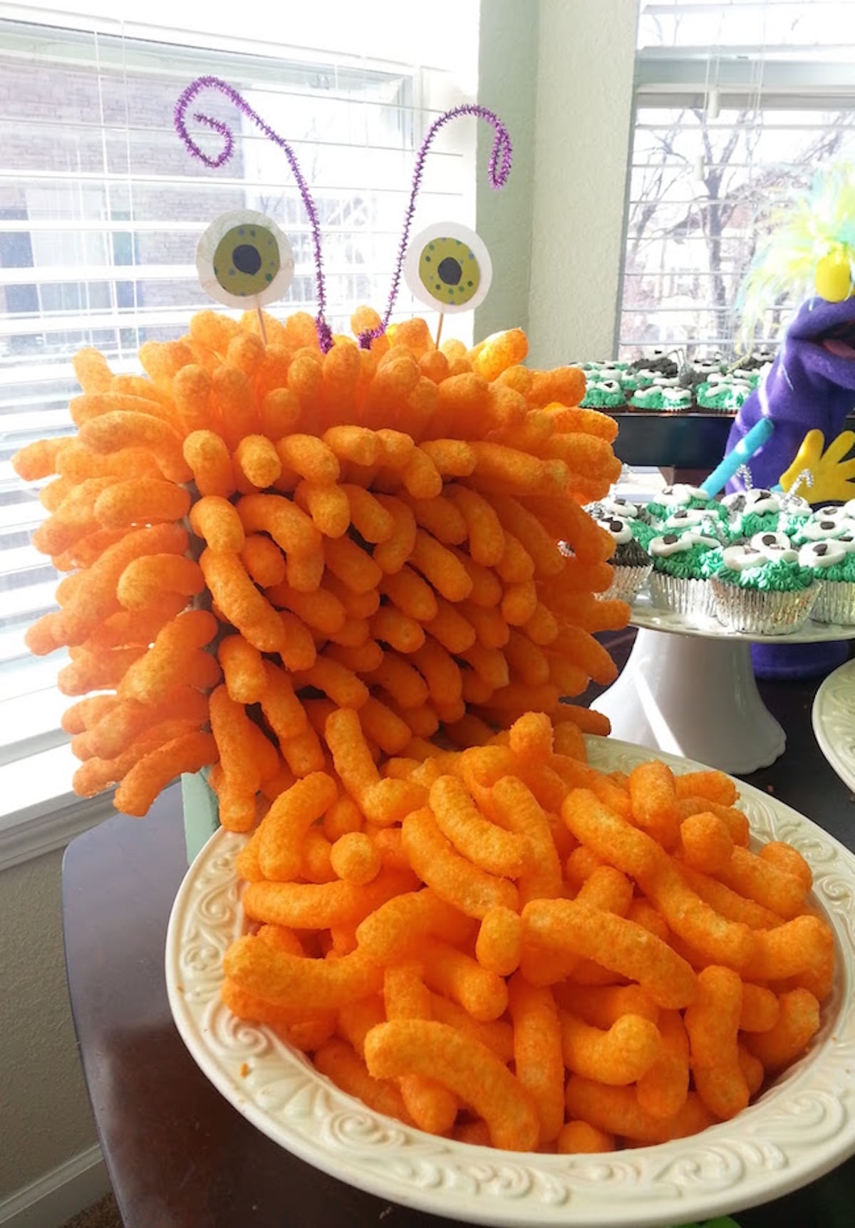Cheeto puffs have been arranged to look like a 3D monster. Paper eyes are affixed to the top of its head with purple pipe cleaner antennas. 