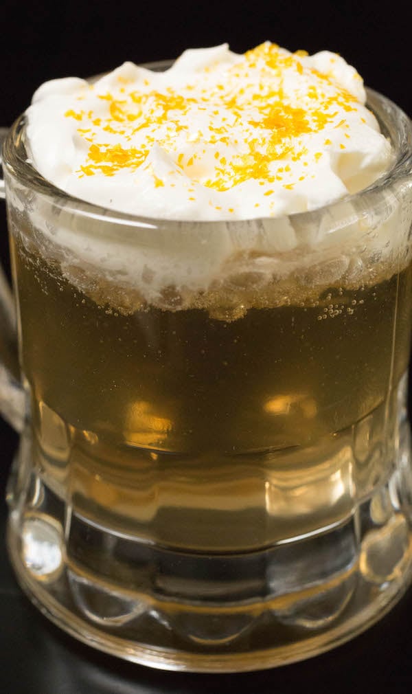 Close up of a butterbeer shot topped with whipped cream and gold glitter.