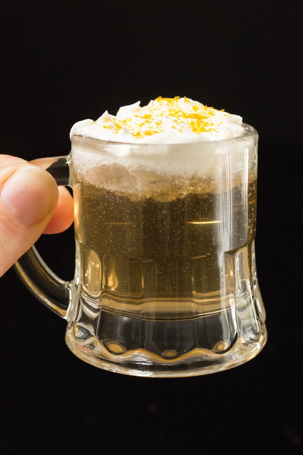 A hand holds up a beer shot glass filled with a butterbeer shot.