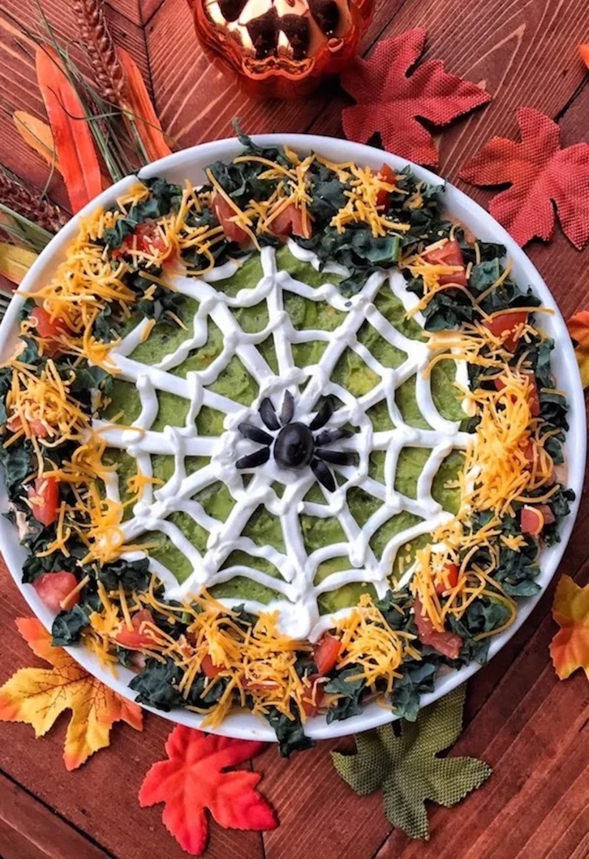 Guacamole is spread on a plate then coated with sour cream to look like a spiderweb. A spider is made in the middle out of black olives.