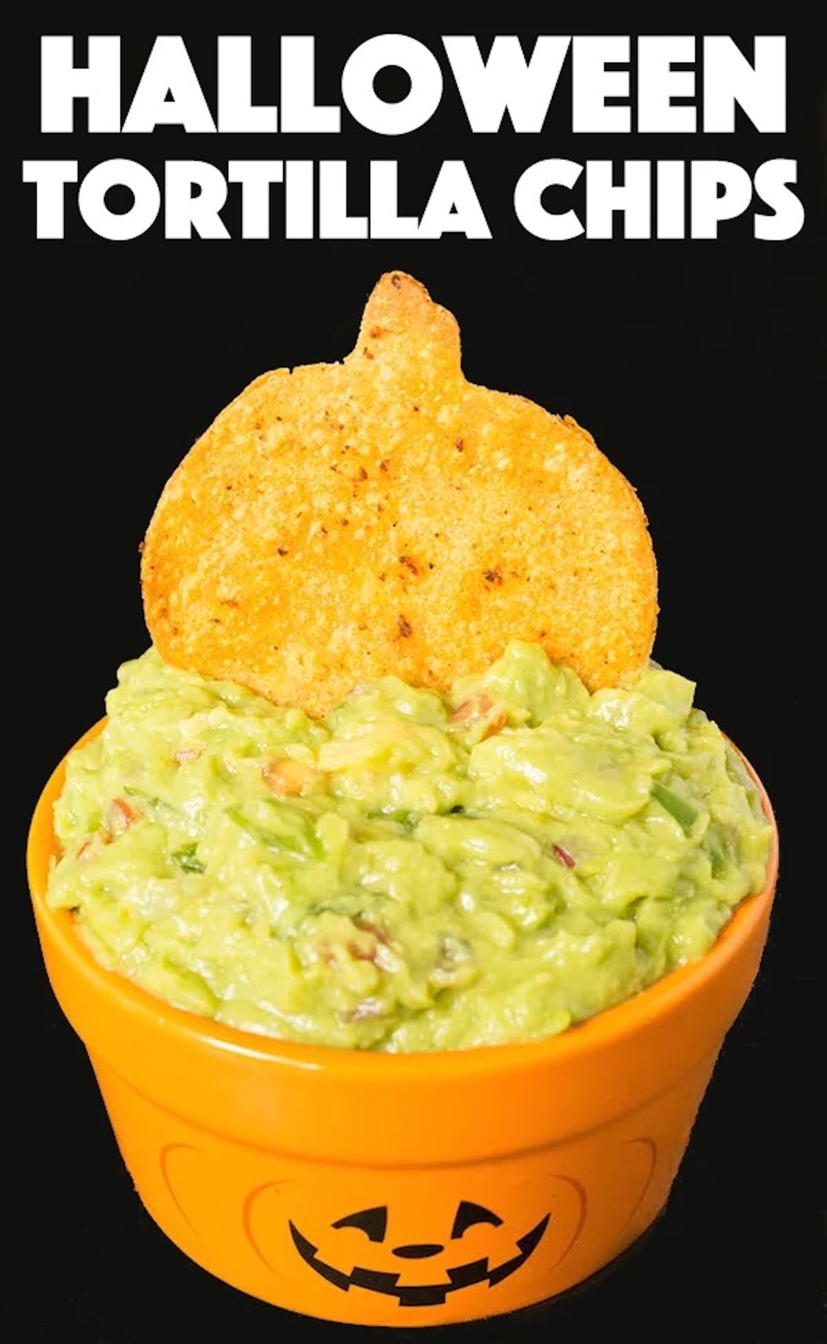 A small pumpkin serving dish is filled with guacamole and topped with a homemade pumpkin shaped tortilla chip.