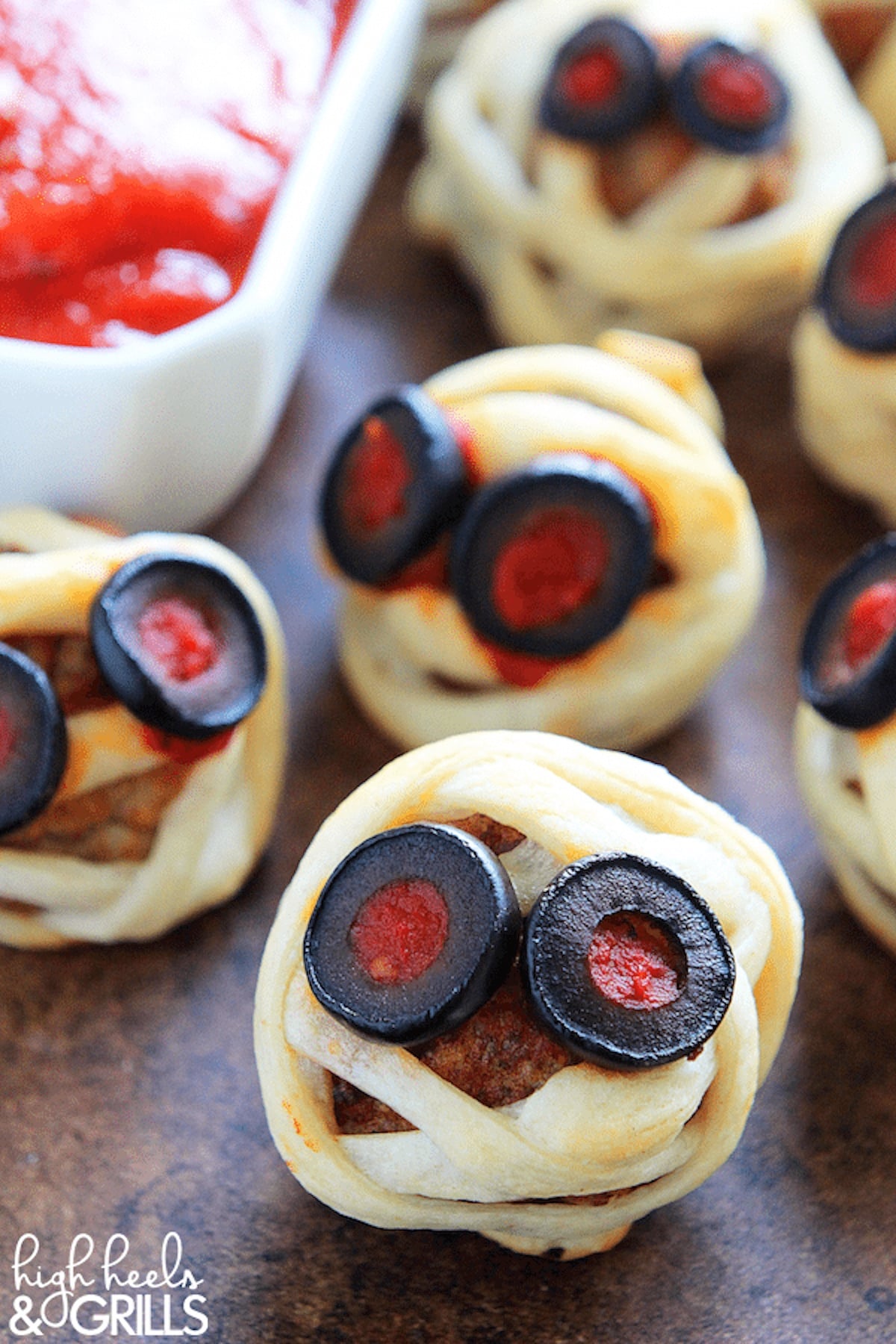 A meatball is covered in puff pastry to look like a mummy and has eyes made of black olives and red sauce.