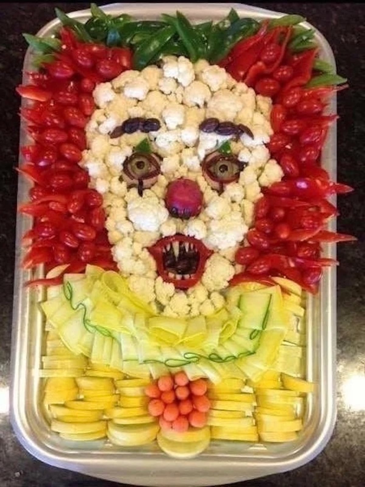 cauliflower, cherry tomatoes, red pepper slices, and ribbons of zucchini and cucumber are arranged to look like the clown from IT.