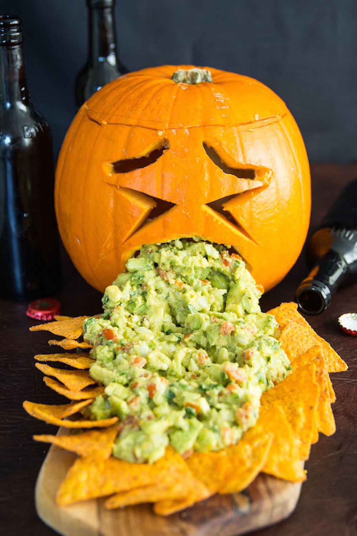 A jack-o-latern has been carved to look like the pumpkin is puking guacamole on to tortilla chips.