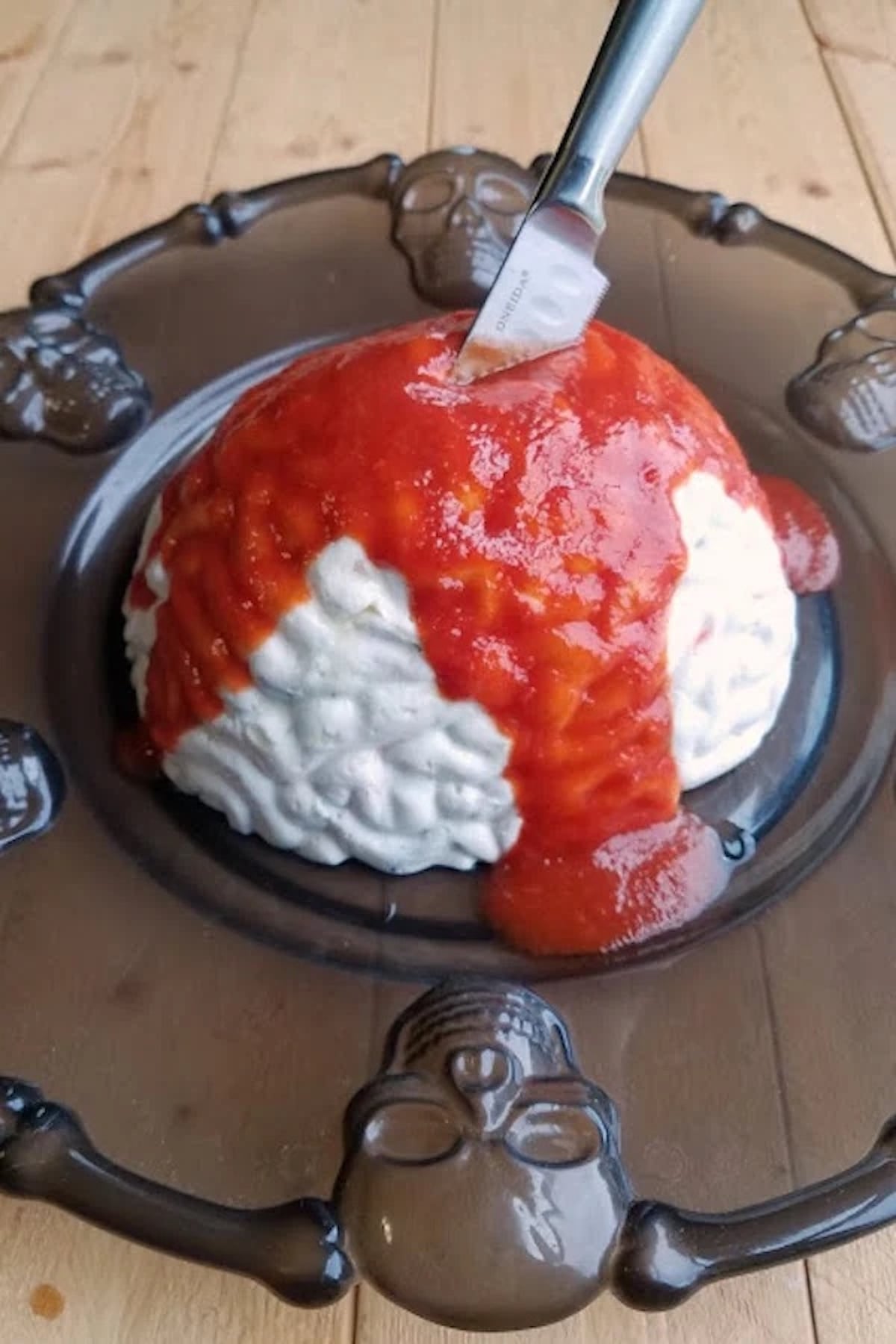 Shrimp dip has been molded into a white brain and topped with a red sauce. A knife sticks out of the top.
