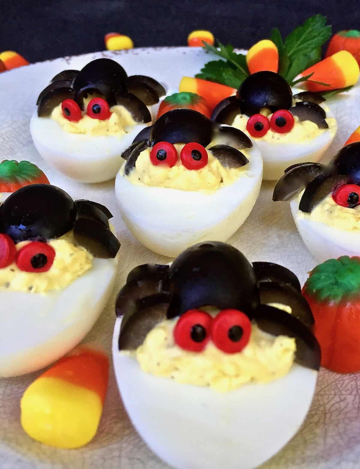 Deviled eggs are topped with black olives arranged to look like spiders and adorned with red candy eyes.
