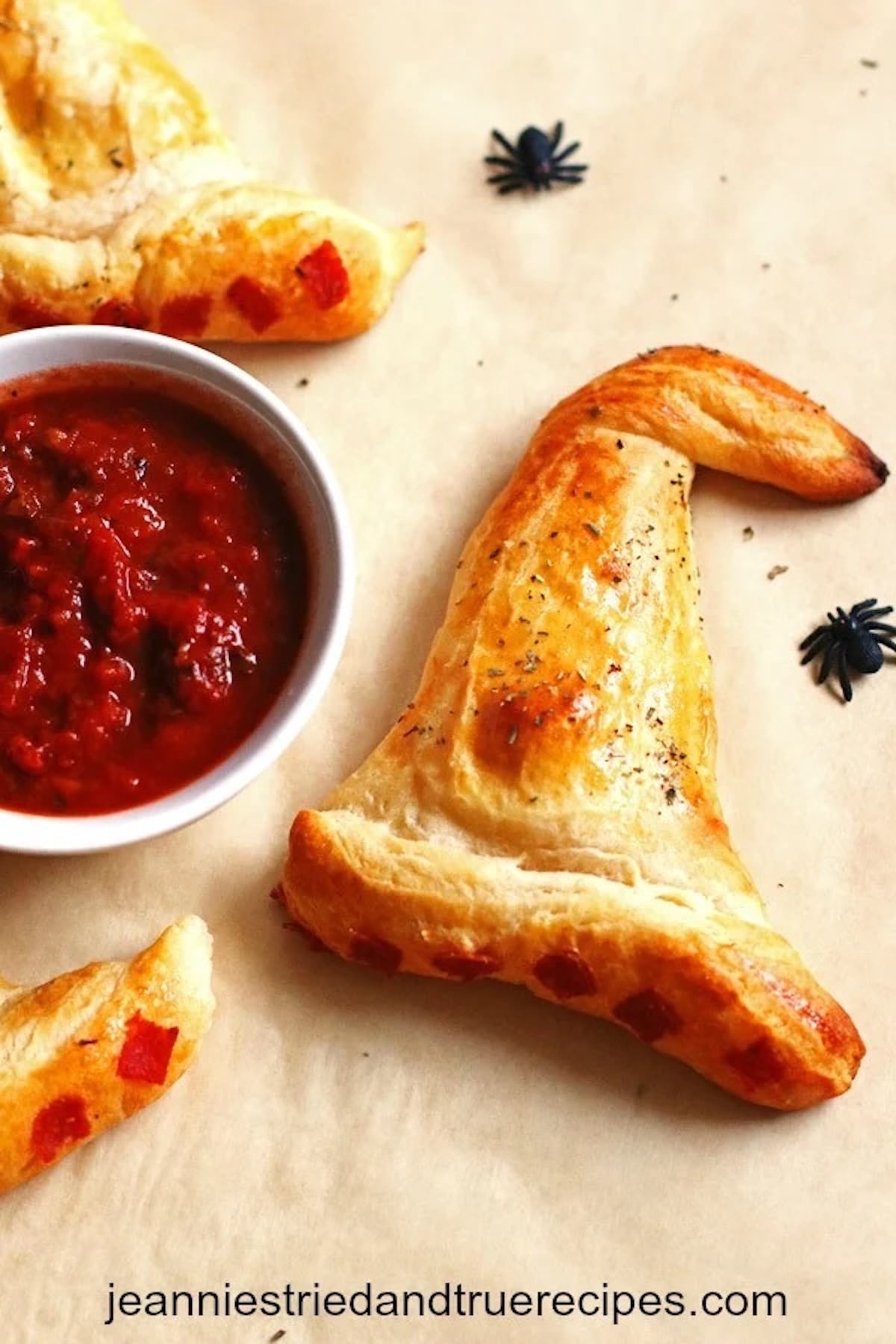 Calzones have been shaped into witch hats and are served next to a bowl of marinara sauce.