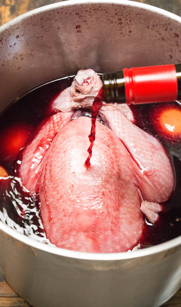 Pouring red wine over a turkey in a stock pot.