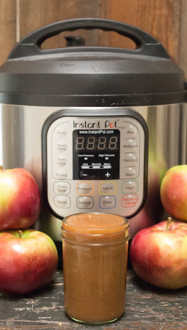 A jar of Instant Pot Apple Butter in front of the appliance and fresh apples.