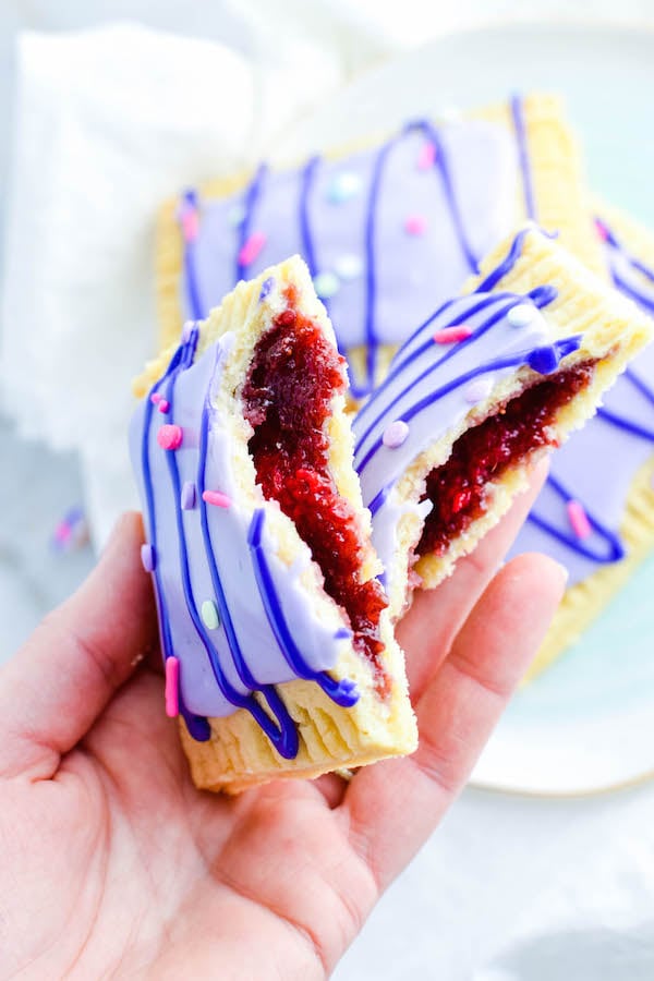Homemade Raspberry Pop-Tarts held up by a hand on a white marble background.