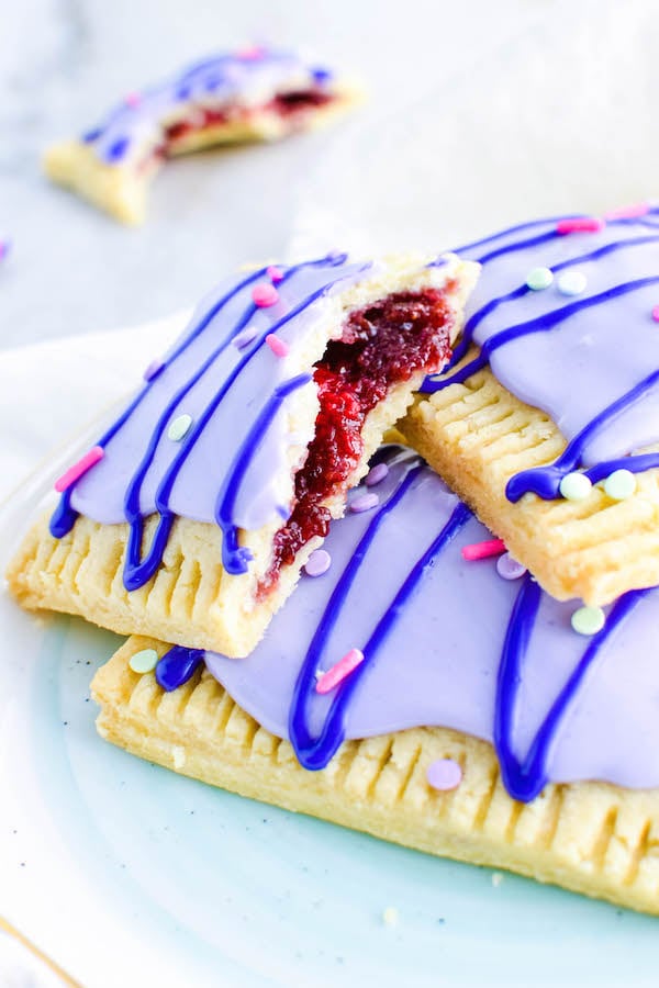 3 Homemade Raspberry Pop-Tarts stacked on a plate. One is cut in half.