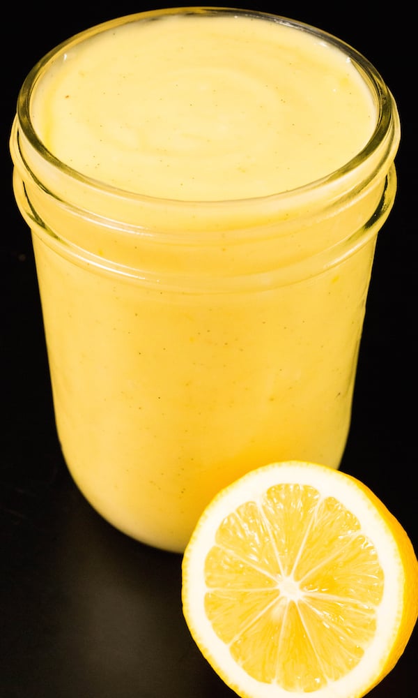 A small glass jar of Meyer lemon curd with a sliced lemon in front of it.
