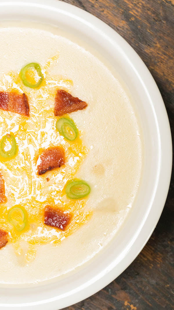 Close-up of Instant Pot Loaded Baked Potato Soup topped with bacon, cheddar cheese, and chives in a white bowl. 